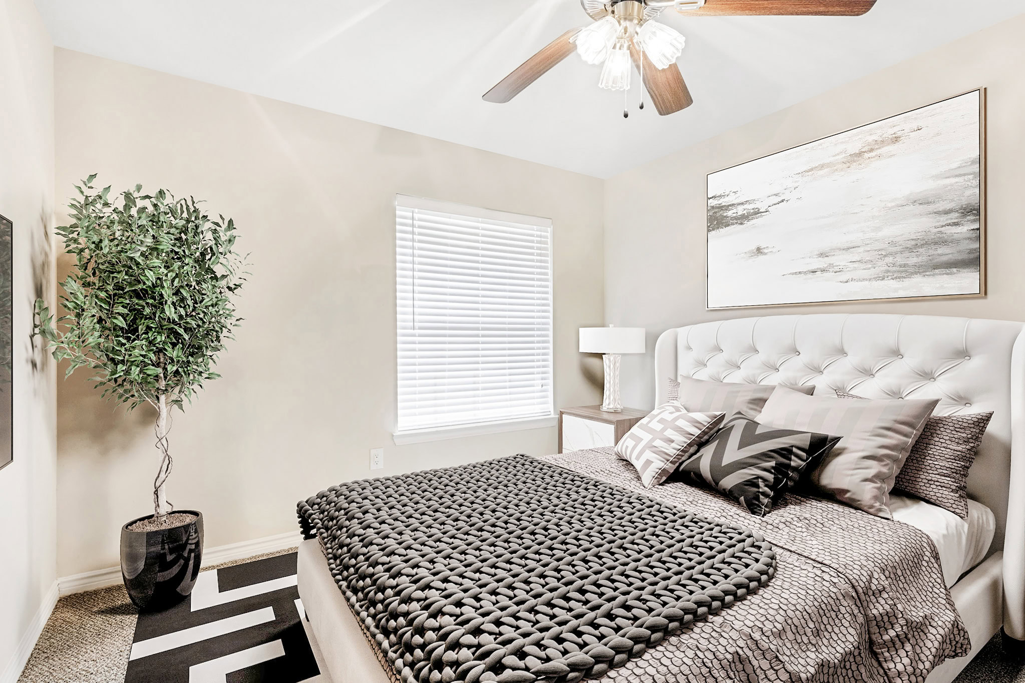 Bright bedroom in a Mckinney Texas apartment featuring a tufted headboard, modern décor, and natural light from a large window.