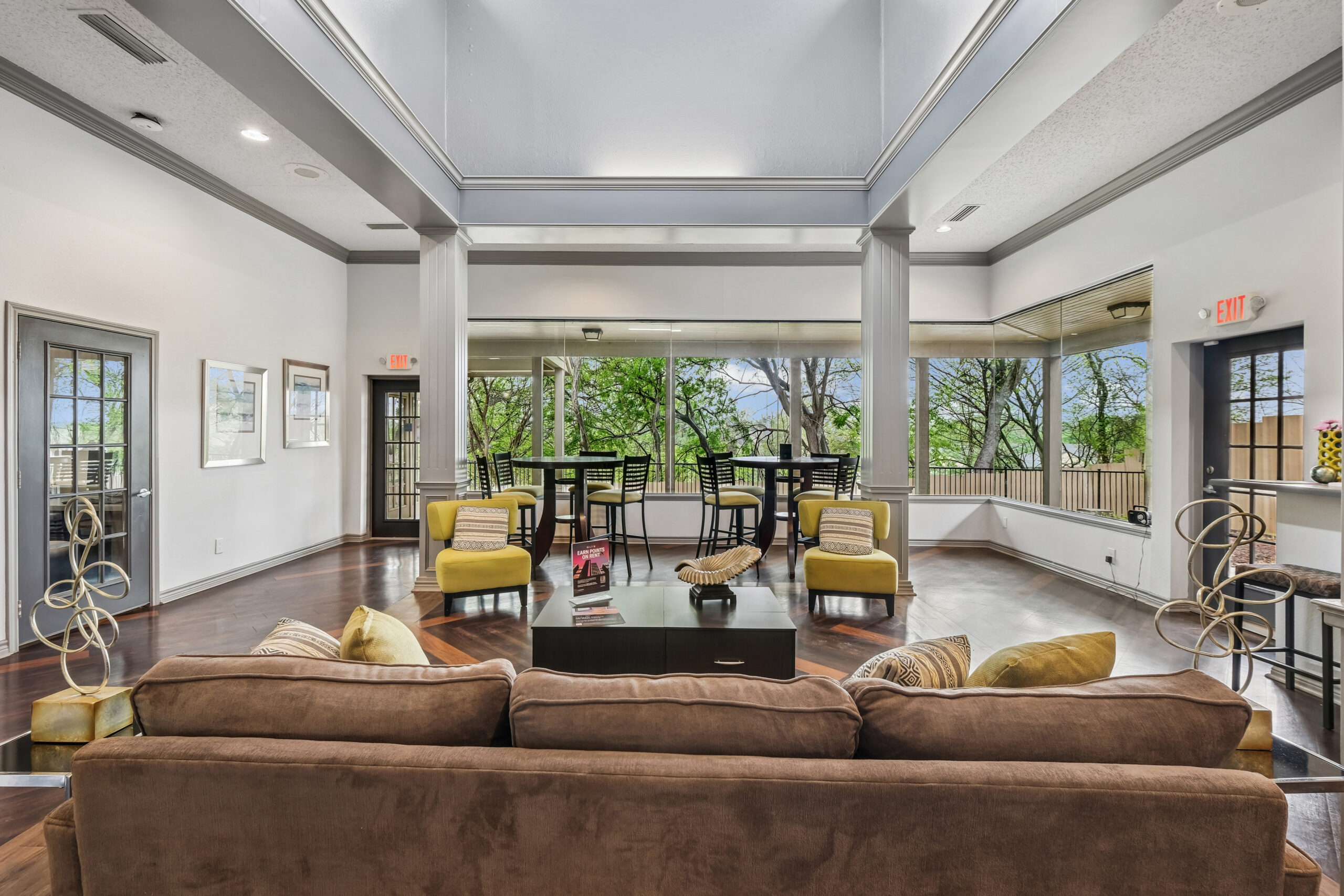 Bright resident clubhouse at the Gables of Mckinney apartments in Mckinney Texas featuring large windows, modern seating, and high ceilings overlooking lush greenery