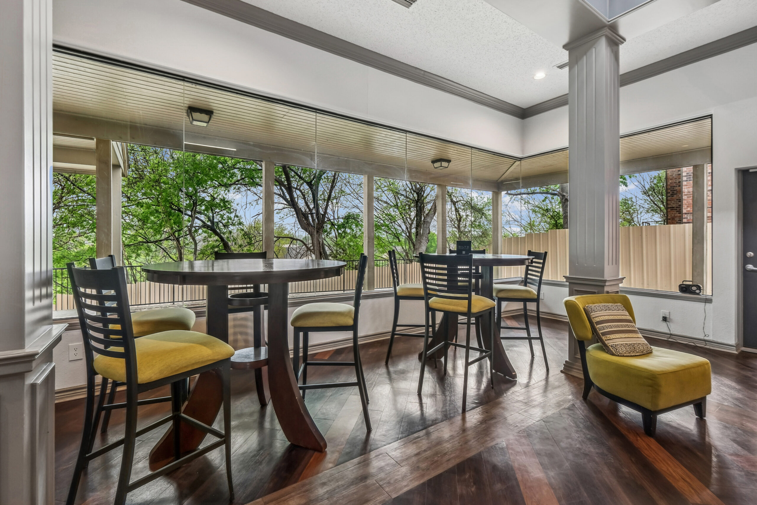 Resident lounge at apartments in Mckinney Texas with tall windows, bar-height tables, and views of lush trees.