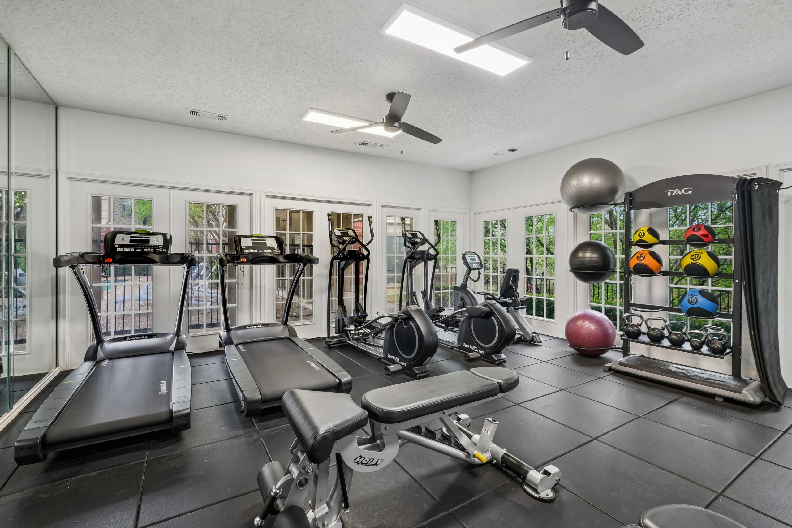 Modern apartment fitness center with treadmills, ellipticals, weight bench, and functional training equipment.