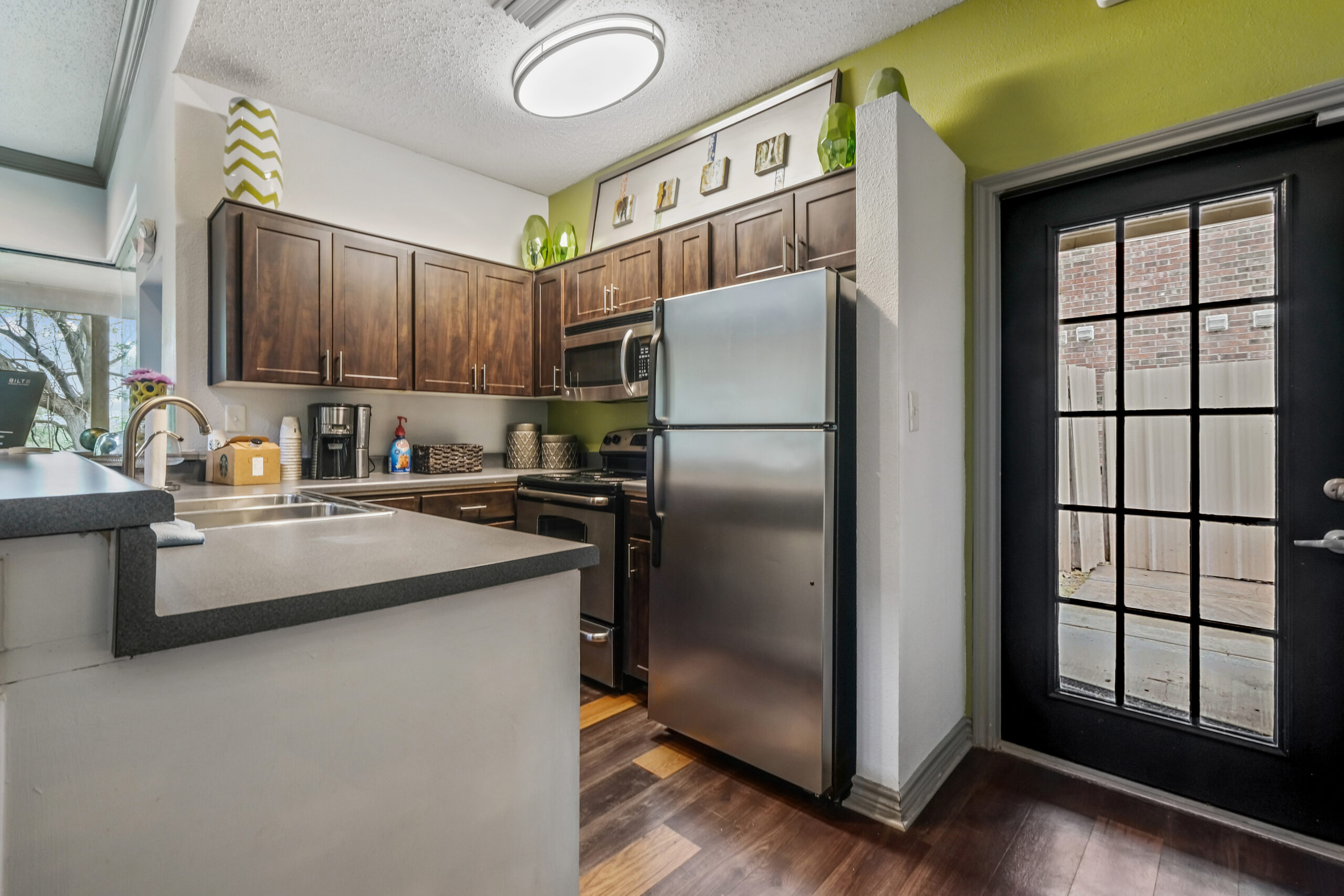 Modern kitchen in Mckinney Texas at the Gables of Mckinney apartments featuring stainless steel appliances, dark wood cabinets, and a private patio door.