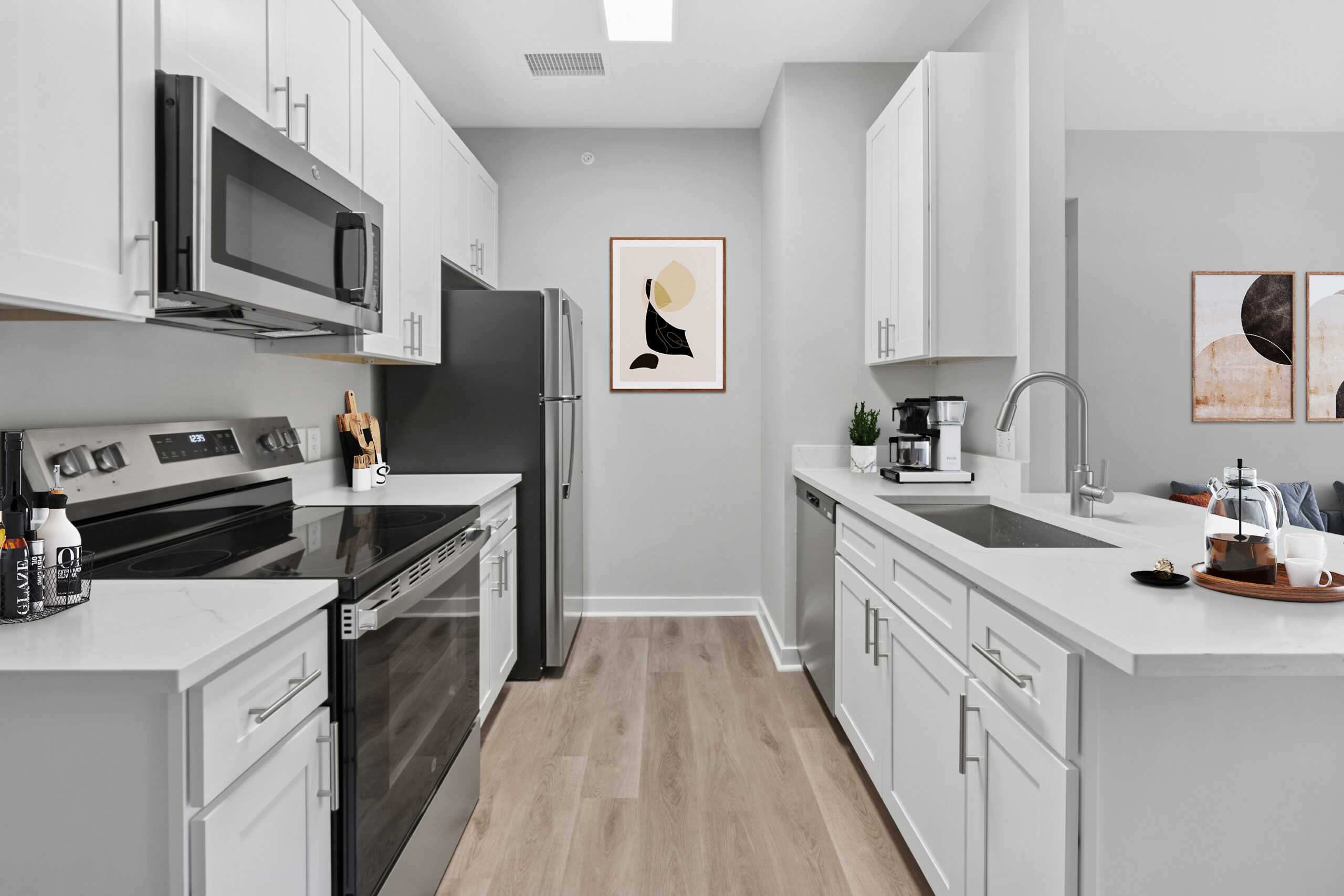 Modern kitchen in a Mckinney Texas apartment featuring white cabinets, stainless steel appliances, quartz countertops, and light wood flooring.