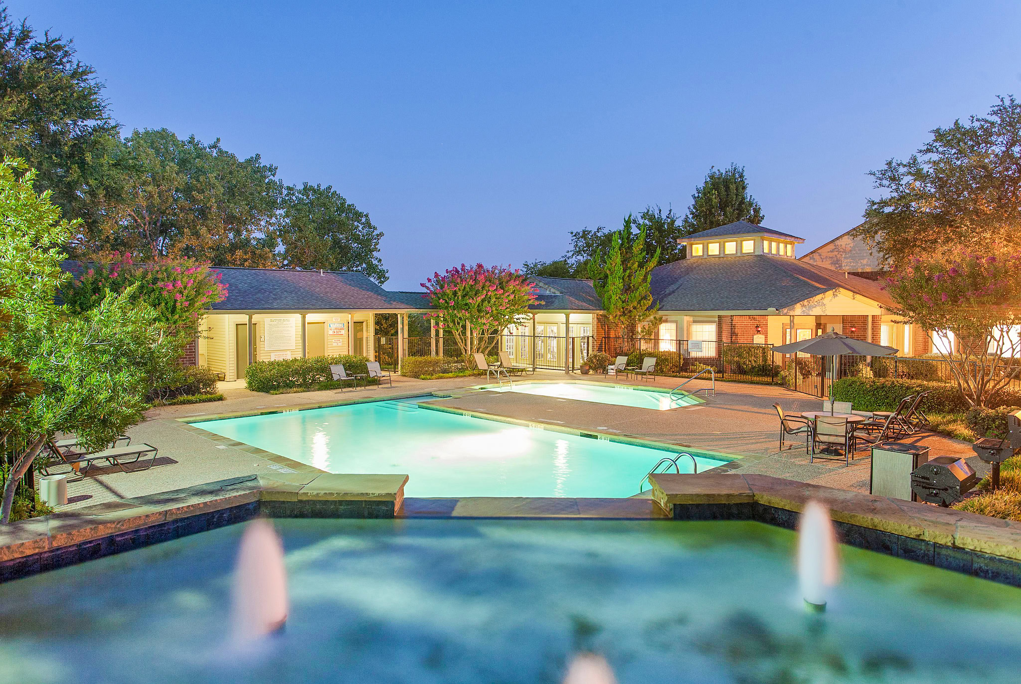 Resort-style pool area at the Gables of Mckinney apartments in Mckinney Texas featuring illuminated swimming pools, lounge seating, and landscaped courtyards.