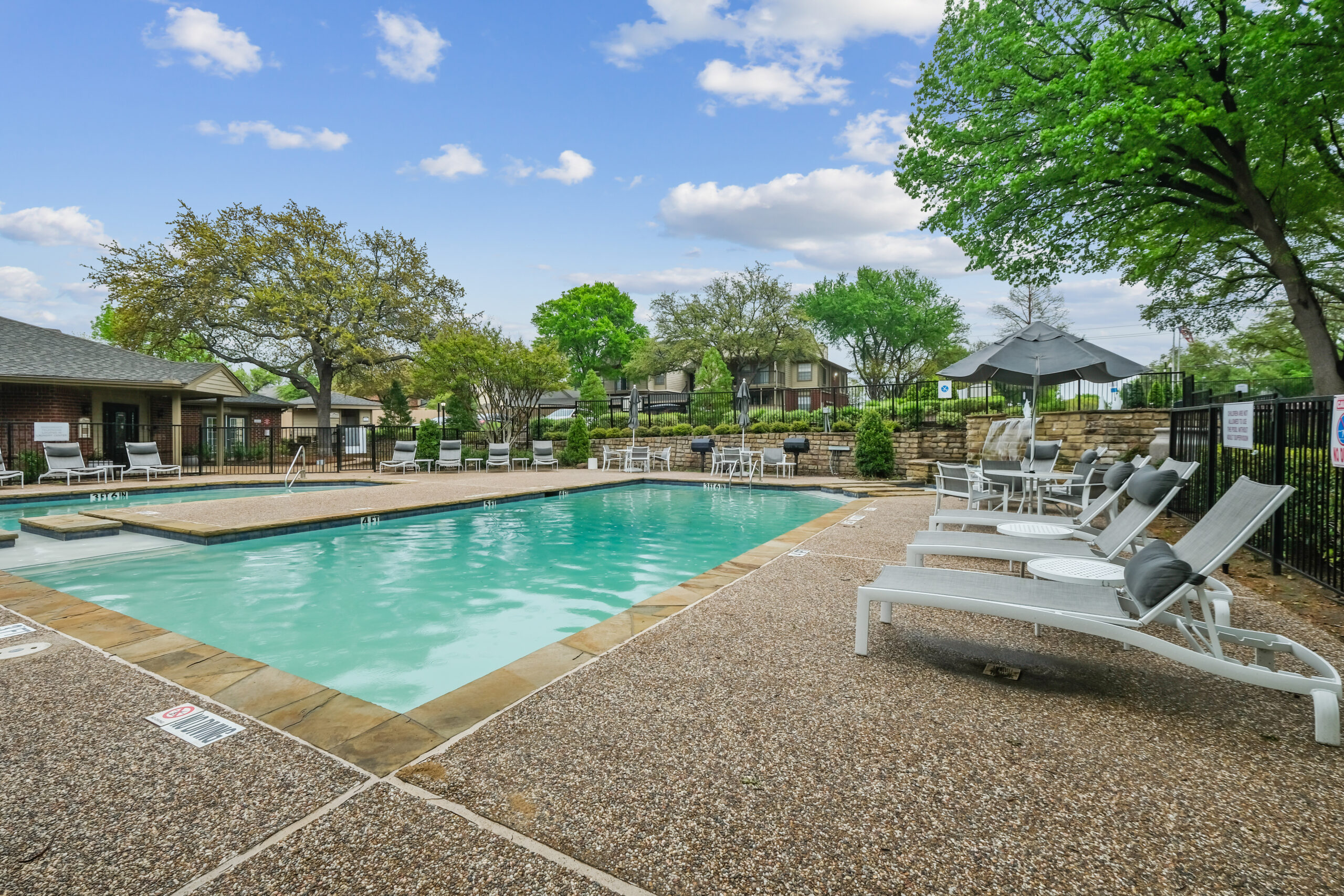 Resort-style swimming pool at Mckinney Texas Gables of Mckinney apartments with sundeck, lounge chairs, and shaded seating.