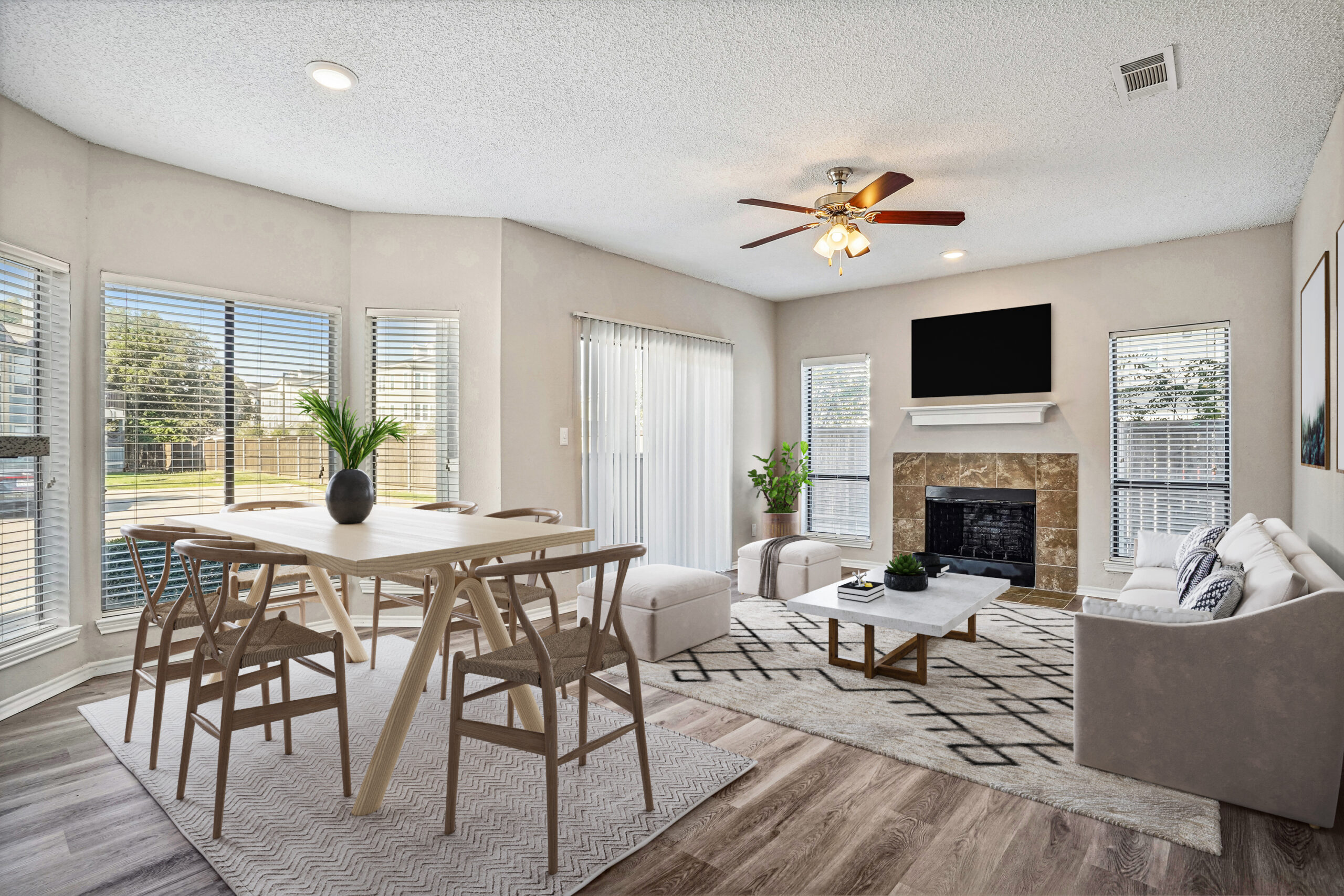Bright open living and dining area in a Garland Texas apartment featuring a fireplace, large windows, and wood-style flooring.