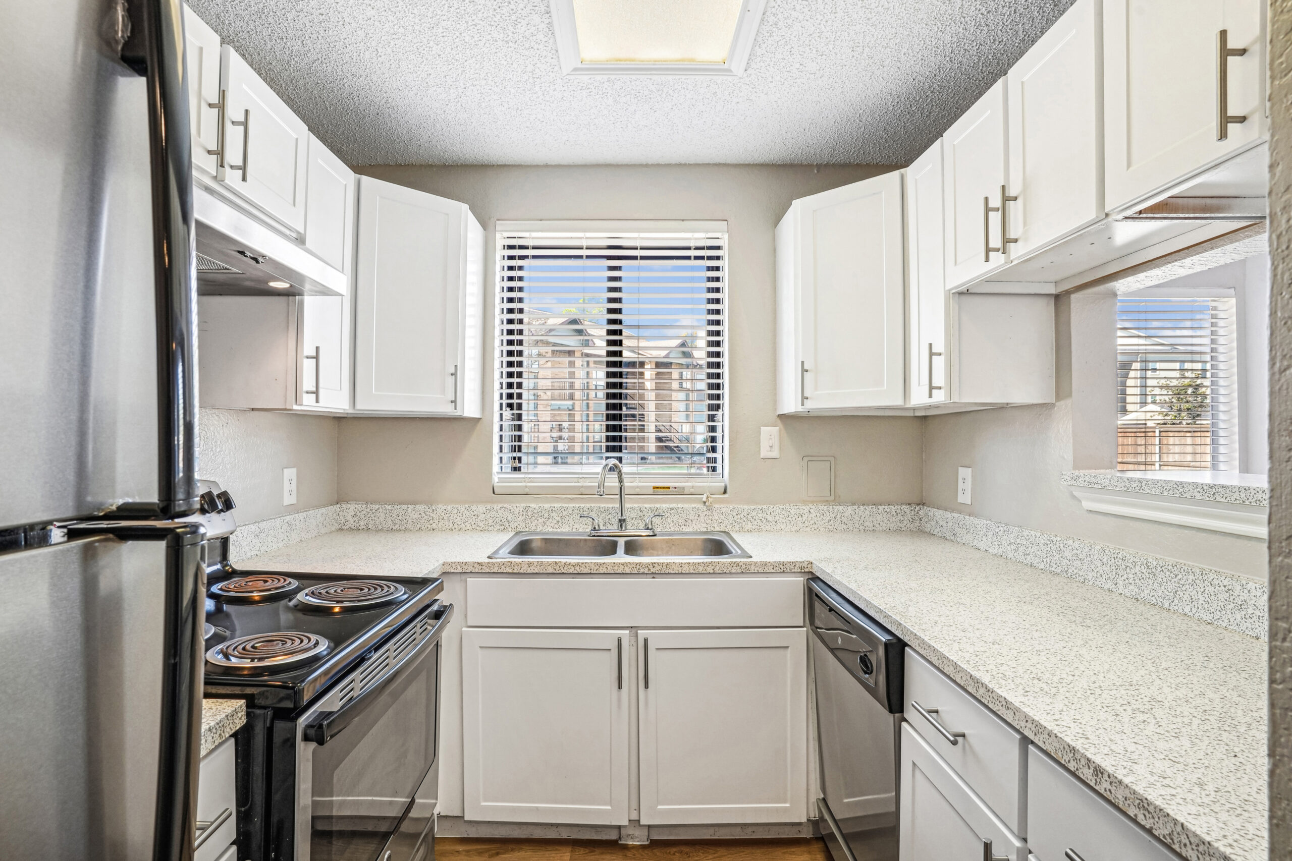 Bright U-shaped kitchen in apartments in Garland Texas with white cabinetry, granite-style countertops, and stainless steel appliances