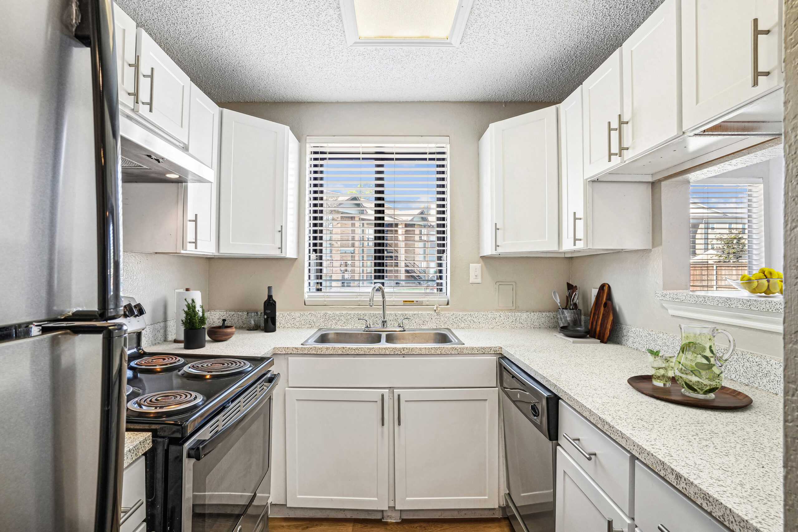 Bright U-shaped kitchen in apartments in Garland Texas with white cabinetry, granite-style countertops, and stainless steel appliances
