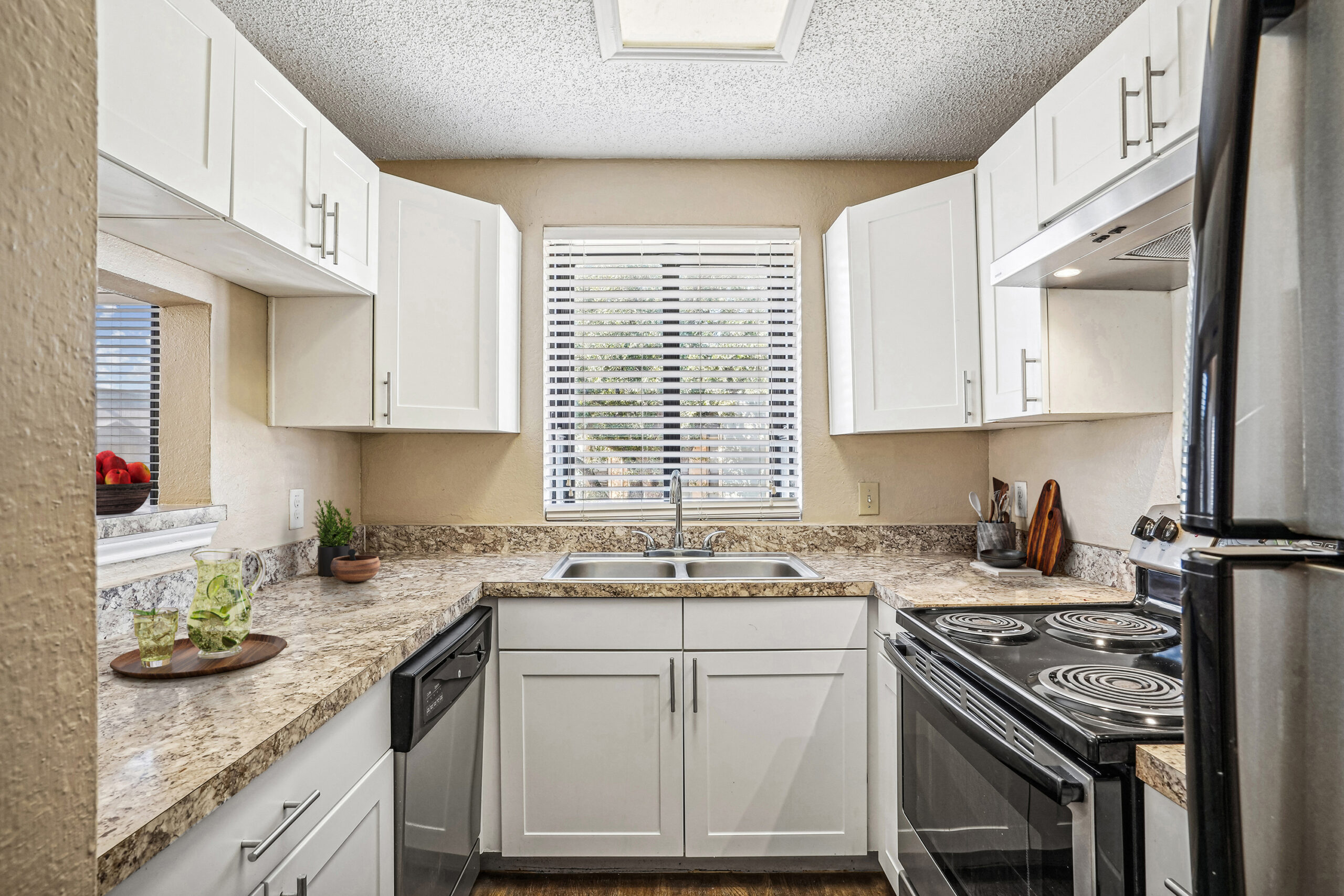 Bright U-shaped kitchen in apartments in Garland Texas with white cabinetry, granite-style countertops, and stainless steel appliances