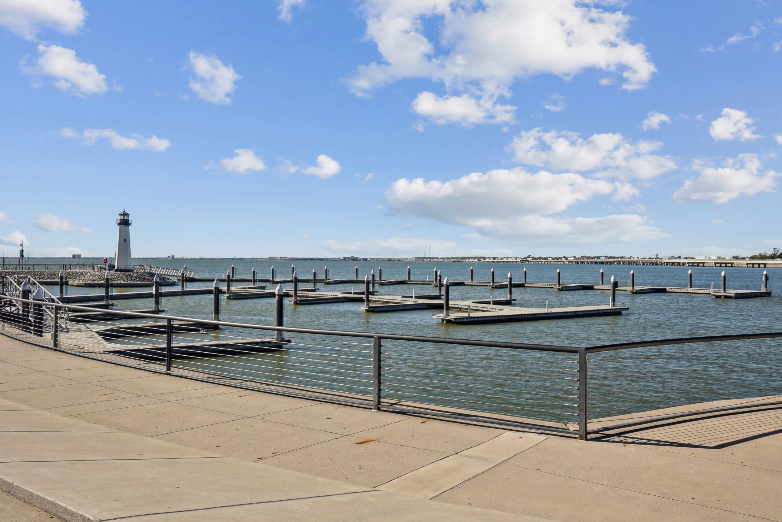 Waterfront marina with empty boat slips and a lighthouse under a bright blue sky near Lake Village West apartments in Garland, Texas