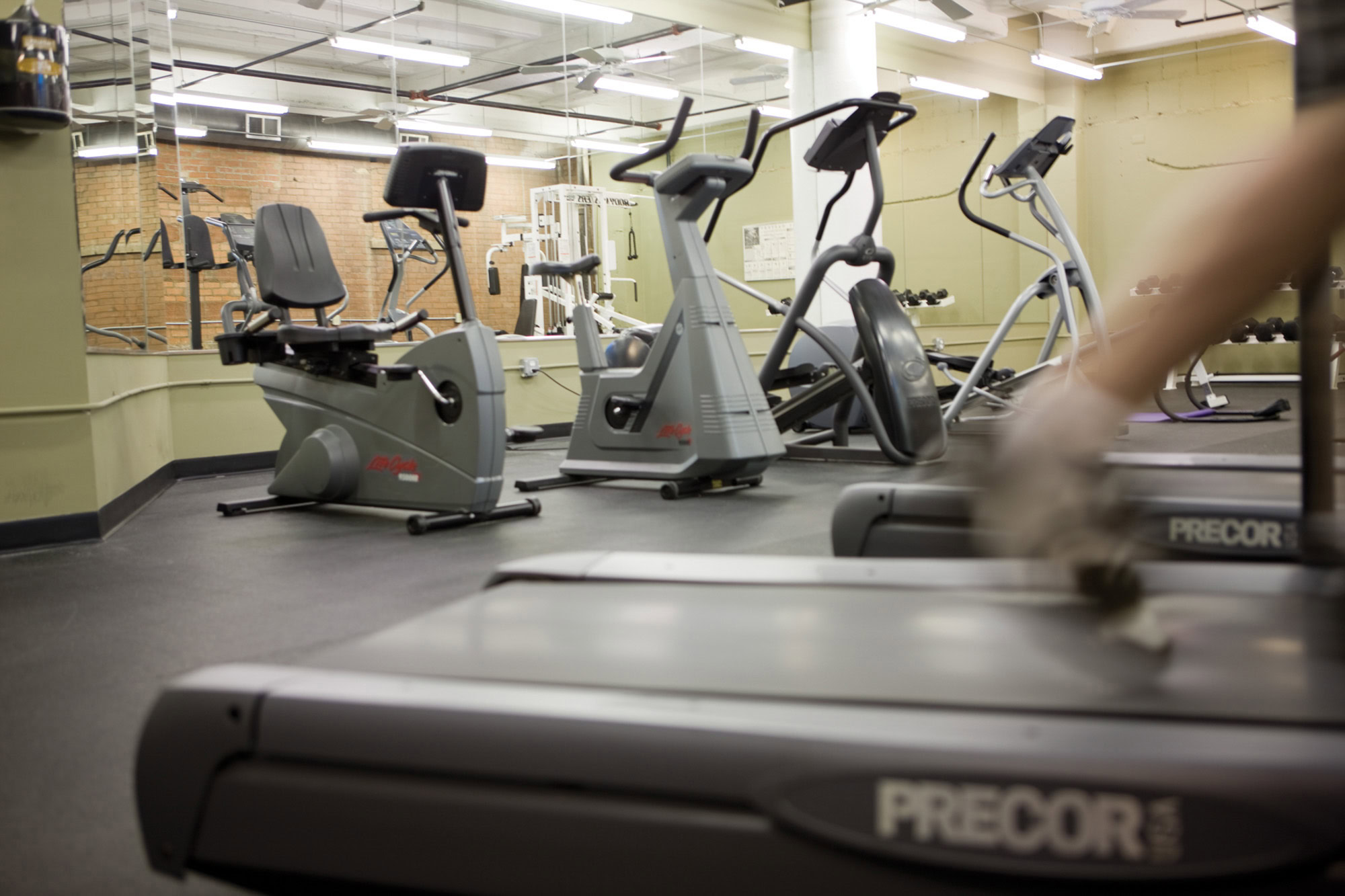 Fitness center with ellipticals, sitting bikes, and a treadmill in use at The Wilson apartments in Dallas, Texas