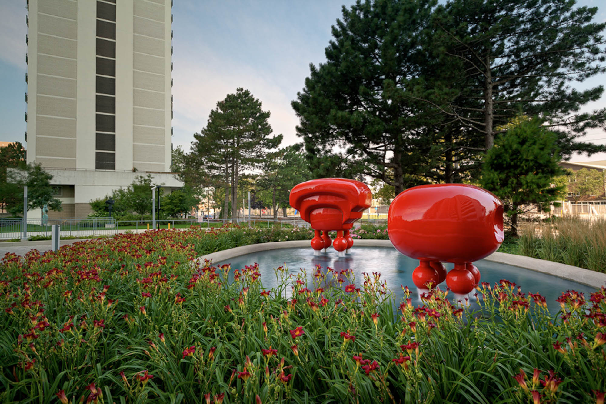 Two red sculptures in a water feature surrounded by a flower garden at the 77 Davisville toronto apartments for rent