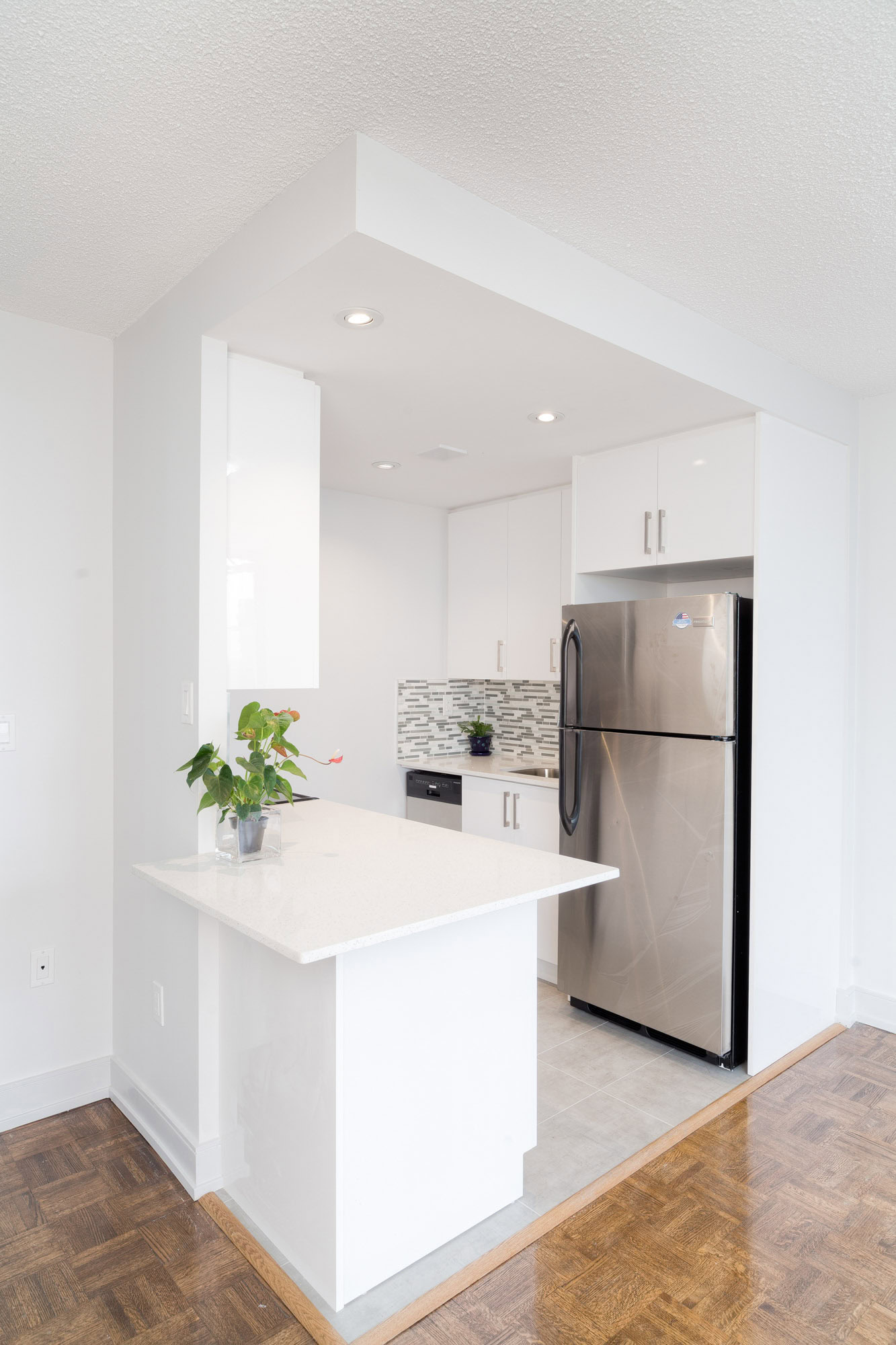 A tiled kitchen with a peninsula island leading to a wood floor living room at the 77 Davisville Toronto apartments