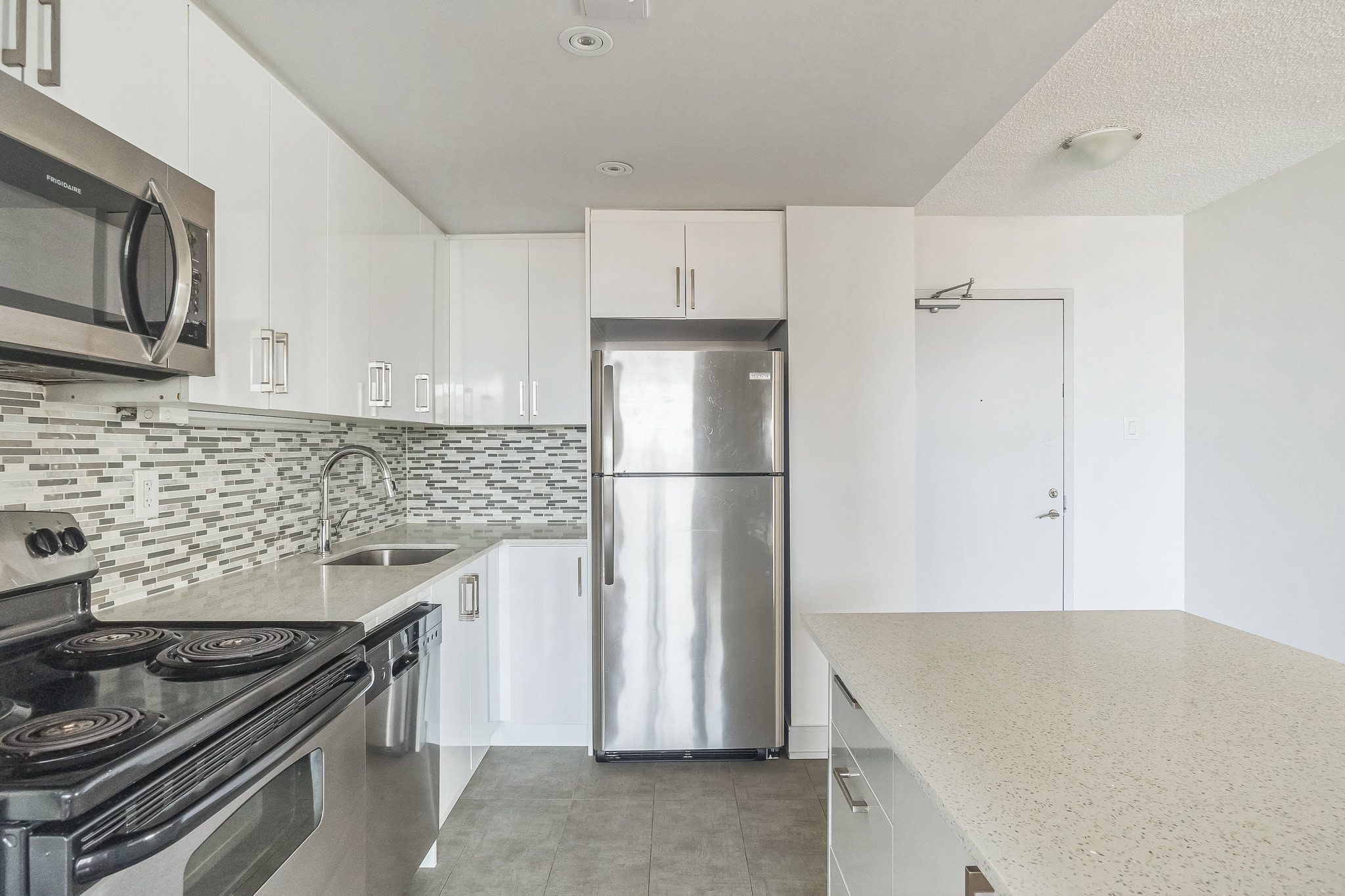 A tiled kitchen with an island and stainless steele appliances at the 77 Davisville apartments in Davisville Toronto