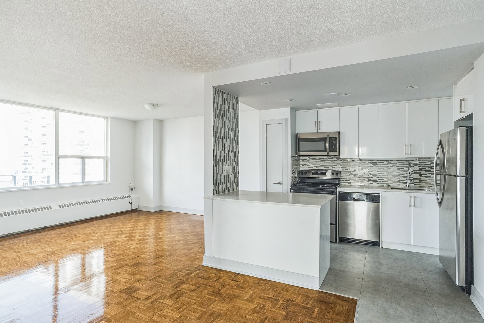 An apartment kitchen with a peninsula, and an open plan dining area and living room with large windows at the 77 Davisville apartments