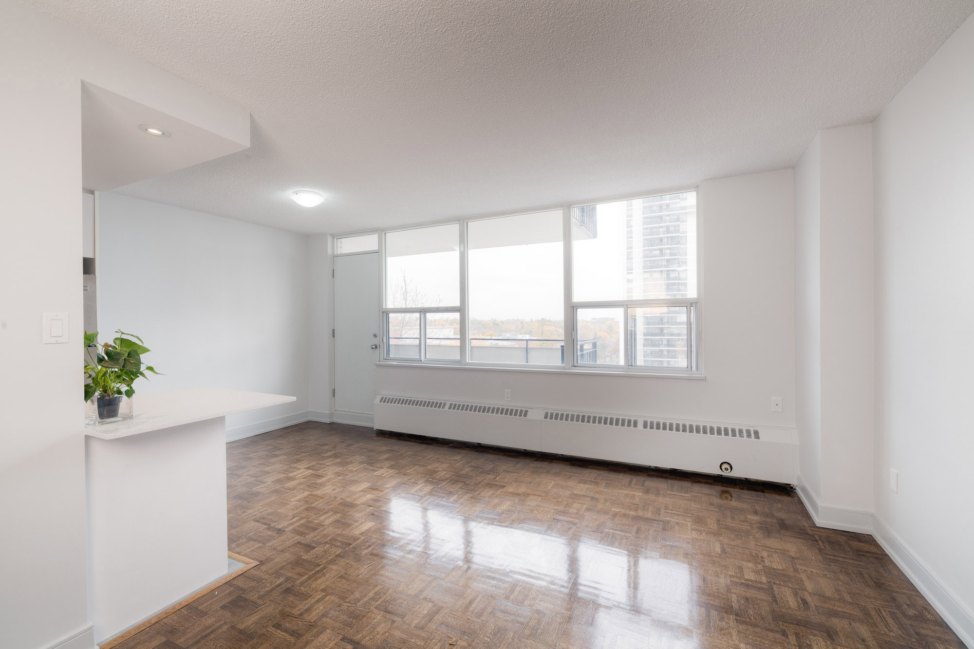 A hard wood floor living room with a large window facing the city at the 77 Davisville apartments for rent in Davisville Toronto