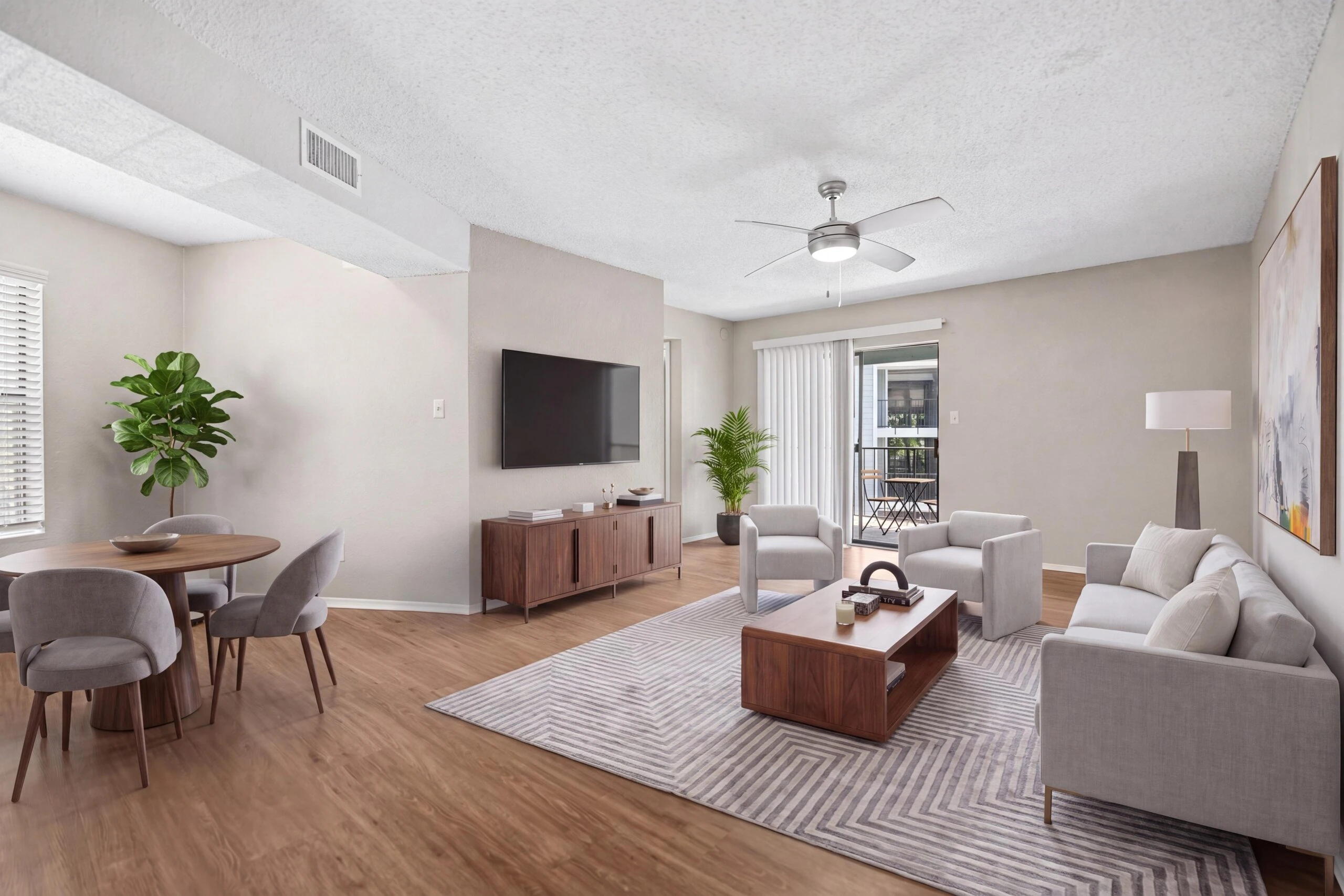 Spacious living room with hardwood plank flooring, ample sunlight, and ceiling fan.