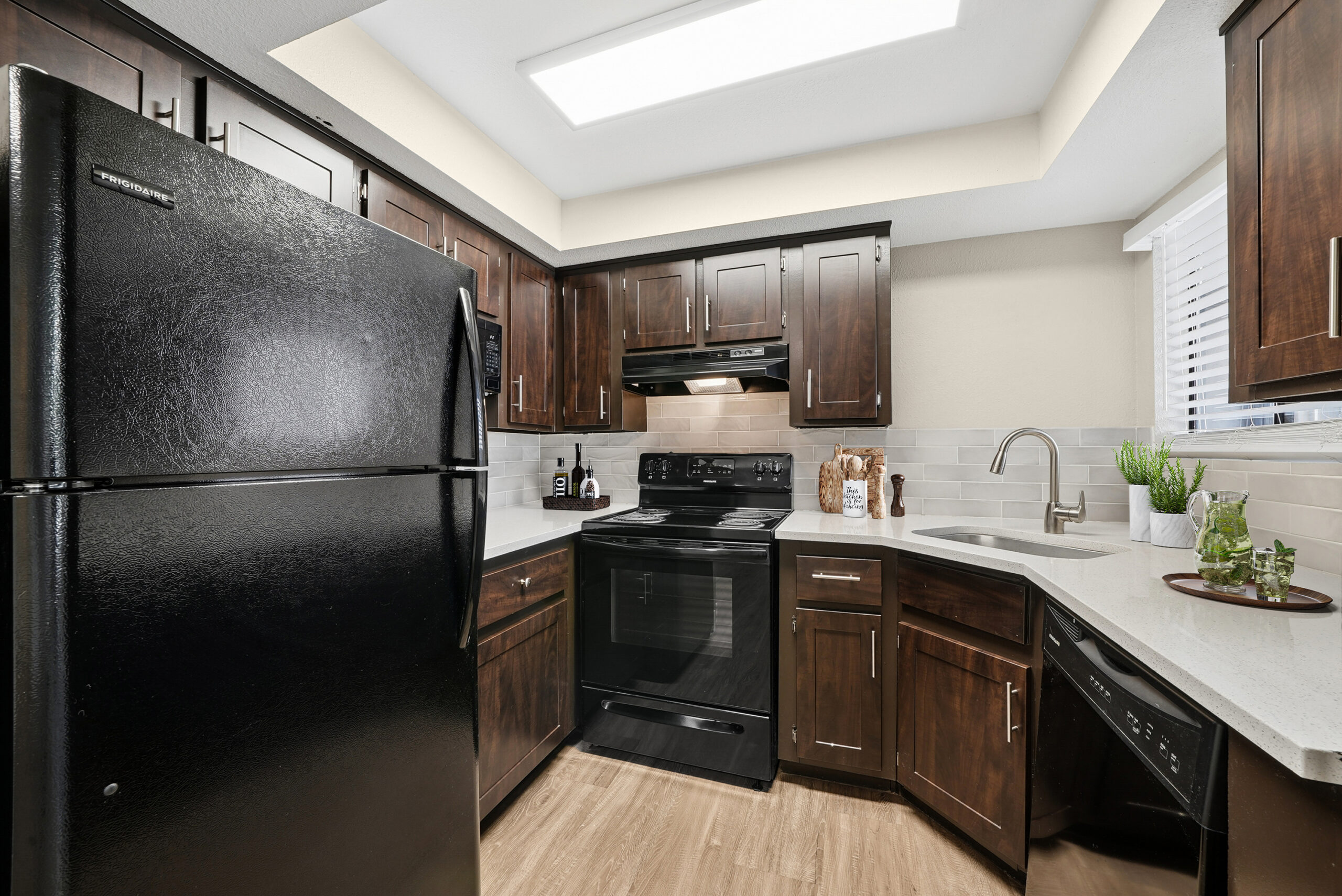 Classic kitchen at Arches at Hidden Creek featuring dark wood cabinetry, light countertops, black appliances and a window above the sink.