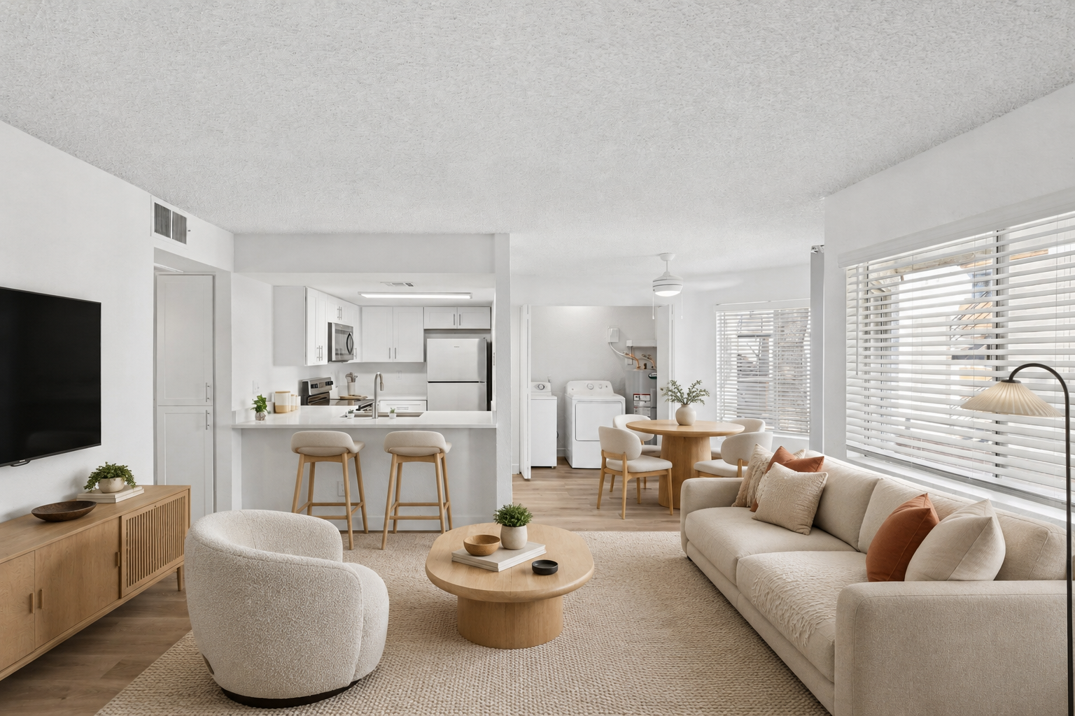 Virtually staged open-concept apartment with a neutral living room, dining area, breakfast bar, stainless steel kitchen, and in-unit laundry.